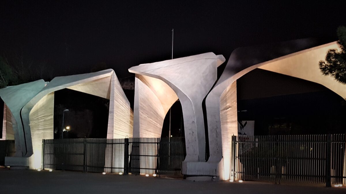 سردر نورپردازی شده دانشگاه تهران در شب پشت نرده های فلزی